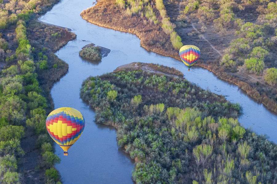 nm-hot-air-balloon-albuquerque 2 brightly colored hot air balloons over the Rio Grande in Albuquerque, NM
